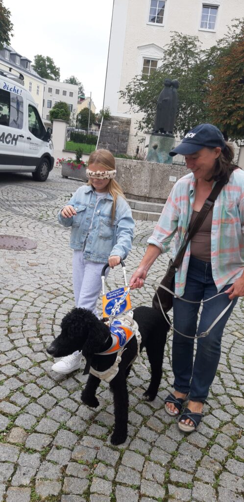 Ein circa 7 jähriges Mädchen geht nit maske über den Augen mit einem Führhund. 